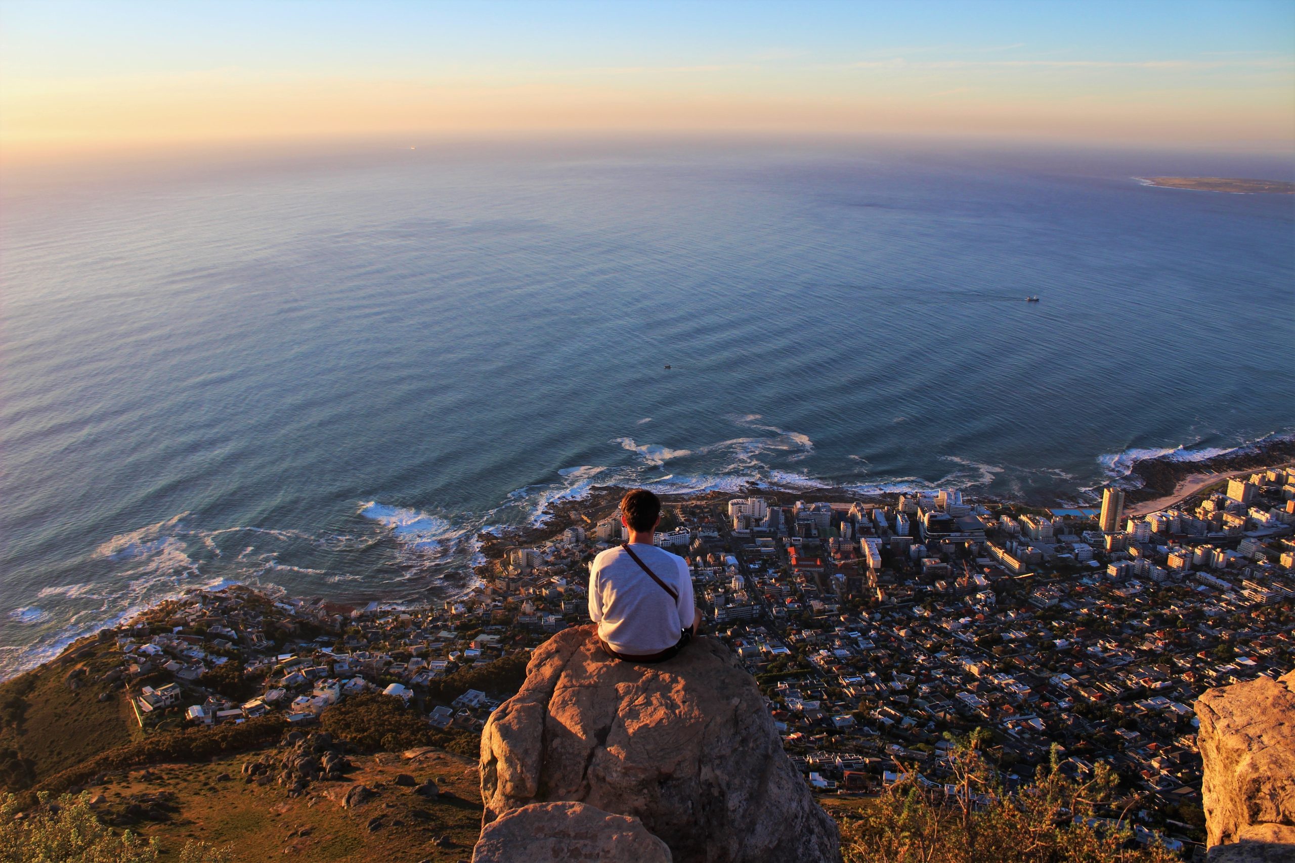 horizontal shot of a man sitting on the edge of the rock and looking at the coastline city